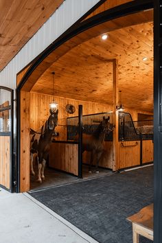 two horses standing in an open stable with wooden walls and doors on either side of them