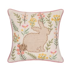 an embroidered pillow with a rabbit on it's side and flowers in the background