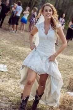 a woman in a white dress and cowboy boots posing for the camera with people behind her