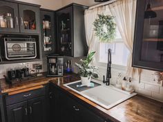 a kitchen with black cabinets and wooden counter tops, white curtains over the window and a potted plant on the sink