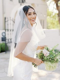 a woman in a wedding dress holding a bouquet and smiling at the camera while wearing a veil