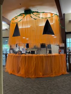 an orange table covered in tulle with black hats on top and green decorations hanging from the ceiling