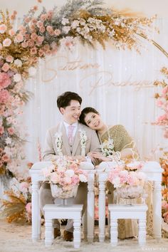 a man and woman sitting at a table in front of a floral backdrop with pink flowers