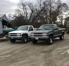 two pickup trucks parked next to each other in front of a barn and tree line