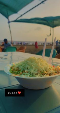 a white bowl filled with coleslaw sitting on top of a table next to an umbrella