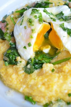 a white plate topped with an egg and greens on top of grits covered in cheese