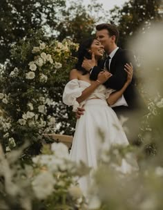 a bride and groom embracing in front of white flowers