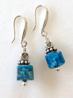 Raw petrol blue apatite earrings with Thai fine silver accents on artisan solid sterling silver ear hooks. Beautiful greenish blue natural apatite faceted gemstone cubes are 9mm and accented with Karen Hill Tribe fine silver triangular beads and sterling silver. Gemstones hang from handmade artisan solid .925 sterling silver ear hooks. Total drop is 1 1/4 inches. Perfect pop of eye catching blue on short artsy ear wires! Turquoise Apatite Gemstone Earrings, Blue Apatite Gemstone Earrings, Handmade Blue Apatite Earrings, Silver Apatite Dangle Earrings, Blue Apatite Earrings For Gift, Blue Apatite Earrings Gift, Blue Earrings For Gift, Turquoise Gemstone Earrings, Aquamarine Earrings