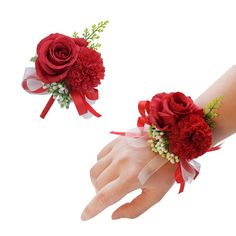 two wrist corsages with red flowers and ribbons on each hand, one being held by someone's hand