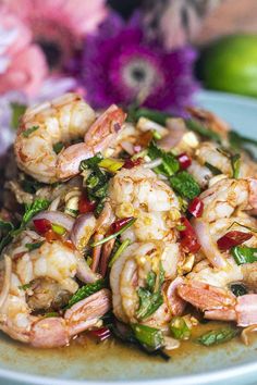 a plate filled with shrimp and vegetables on top of a table next to some flowers