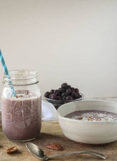 there is a bowl of blueberries and a glass of smoothie on the table