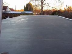 an empty flat roof in front of a house with trees and bushes behind it at sunset