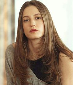 a woman with long brown hair wearing a gray shirt and black top looking off to the side