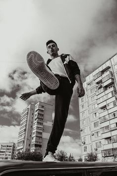 a man holding a tennis racquet on top of a car in front of tall buildings