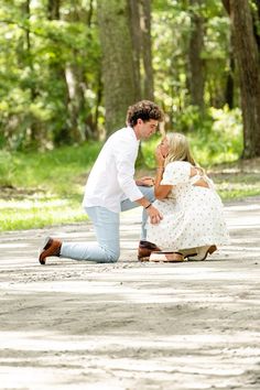 a man kneeling down next to a woman on the ground with trees in the background