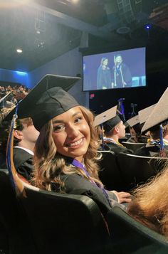 a woman wearing a graduation cap and gown sitting in front of a large screen at a graduation ceremony