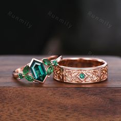 two gold rings with emeralds and diamonds sitting on top of a wooden table next to each other