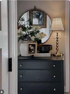 a black dresser with flowers and pictures on it in front of a round mirror above the dresser