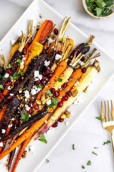 roasted carrots with herbs and feta cheese on a white plate next to a gold fork