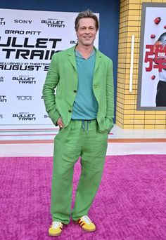 a man in green suit and yellow shoes standing on pink carpet at the movie premiere