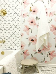 a white bath tub sitting next to a wall with pink flowers on it and a gold faucet