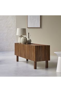 a table with two vases on it next to a white chair and wall in the background