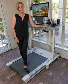 a woman standing on a treadmill in front of a large window with a computer