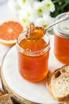 a jar of jam on a plate with bread and grapefruits in the background