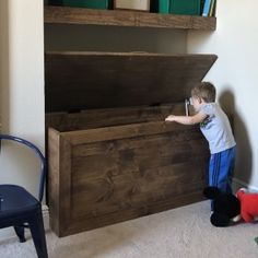 a little boy standing next to a wooden chest