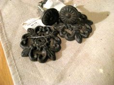 two pairs of black earrings sitting on top of a piece of cloth next to a pair of scissors