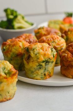 several small muffins on a plate with broccoli and carrots in the background