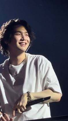 a young man holding a microphone in his right hand and wearing a white shirt on stage