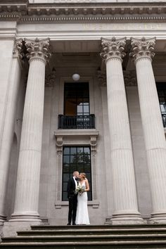 a bride and groom standing on the steps of an old building with columns in front of them