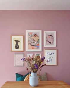 a vase with flowers sitting on top of a wooden table in front of framed pictures