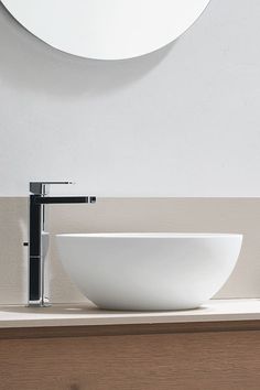 a white bowl sink sitting on top of a wooden counter next to a round mirror