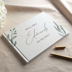 a wedding guest book and pen sitting on a table with flowers in front of it