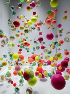 an art installation with colorful balls floating from the ceiling to the floor in front of a white wall