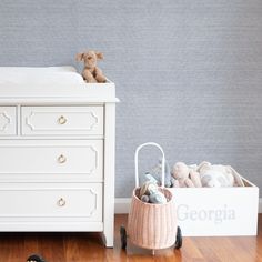 a teddy bear sitting on top of a white dresser next to a baby crib