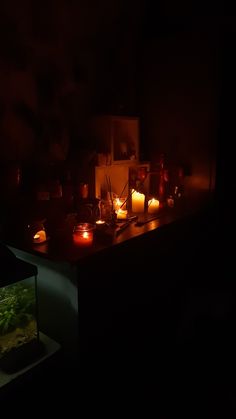 many candles are lit in the dark near a fish tank