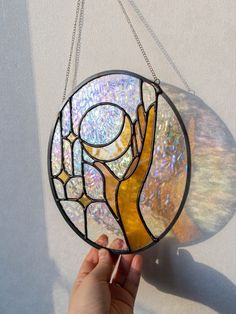 a hand holding up a stained glass window hanging from a chain on a white wall