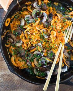 a skillet filled with carrots and mushrooms on top of a wooden table next to a napkin