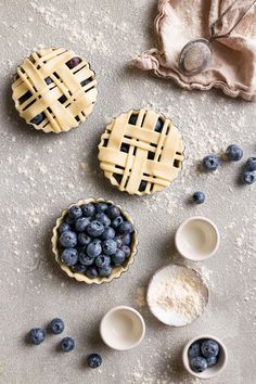 three pies with blueberries and powdered sugar on the table next to them