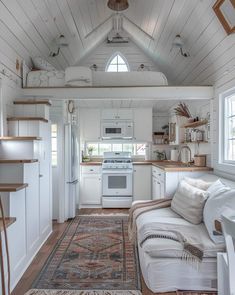 a white kitchen and living room in a tiny home with wood floors, vaulted ceilings, and an area rug on the floor