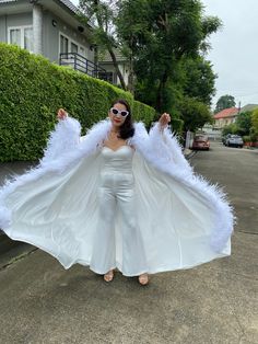 a woman in white is standing on the street with her arms out and wings outstretched