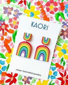 a pair of rainbow earrings on top of a colorful flowered background with the word kaori written in large letters