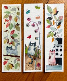 three bookmarks with cats and flowers on them sitting on a wooden table next to each other