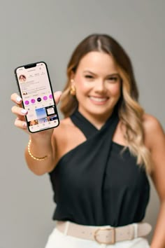 a woman in a black top is holding up her cell phone and smiling at the camera