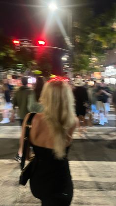 a woman is walking down the street at night with her back turned to the camera