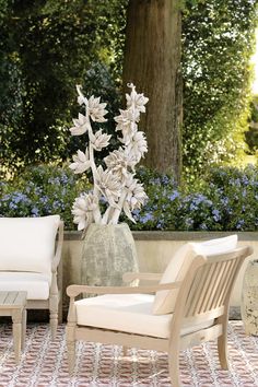 two chairs and a vase with flowers in it on a tiled floor next to a tree