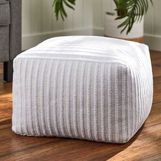 a white ottoman sitting on top of a wooden floor next to a potted plant